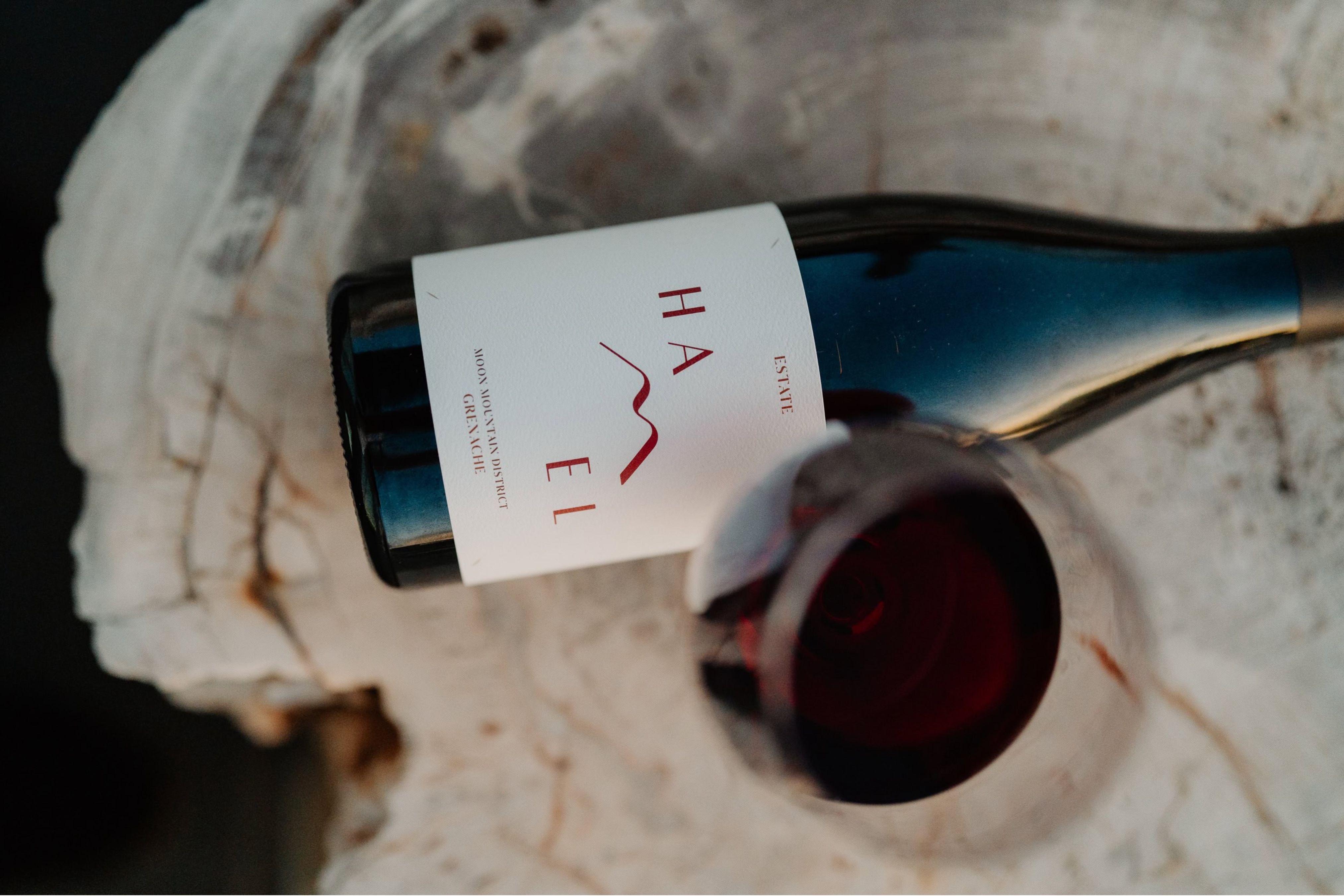 Bottle and glass of Estate Moon Mountain District Grenache on a contemporary tree-stump tabletop.