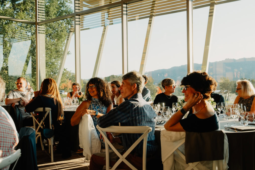 People in sunlit room sitting around tables with wine glasses.